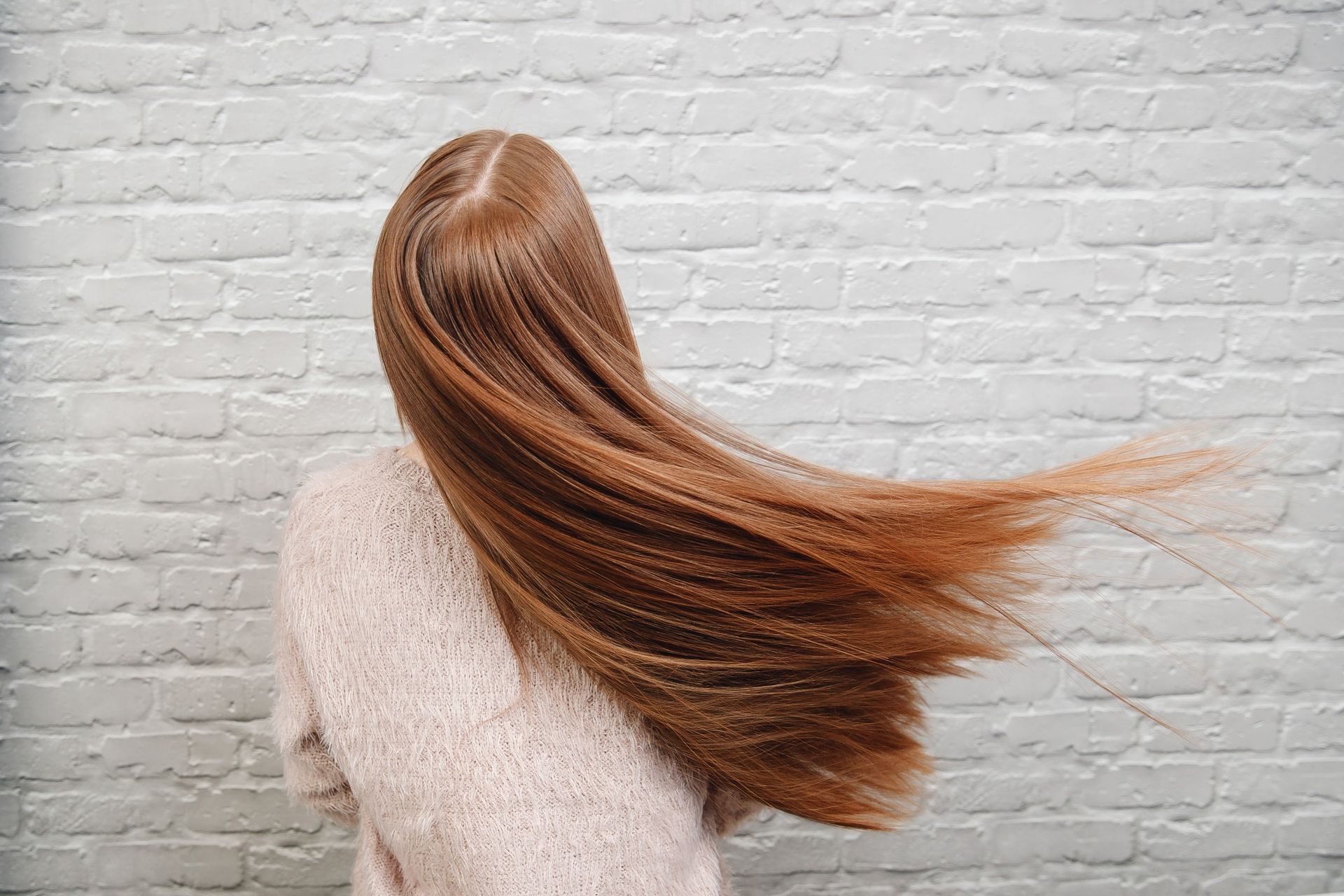 Una mujer con cabello largo y rojo está parada frente a una pared de ladrillos blancos.