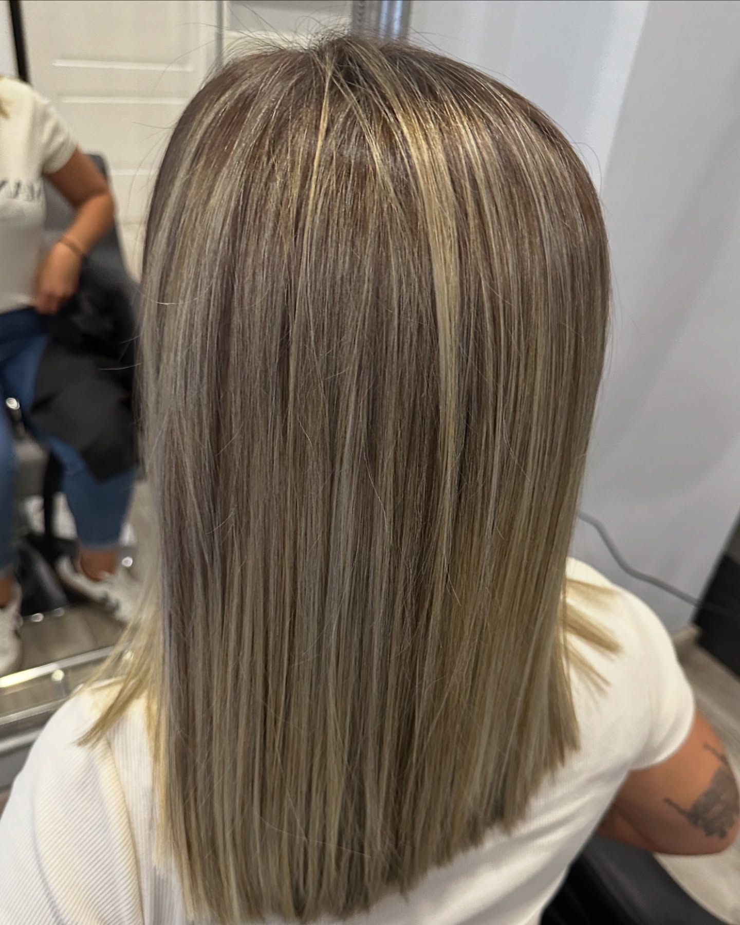 Una mujer con cabello largo y rubio está sentada en una silla frente a un espejo.