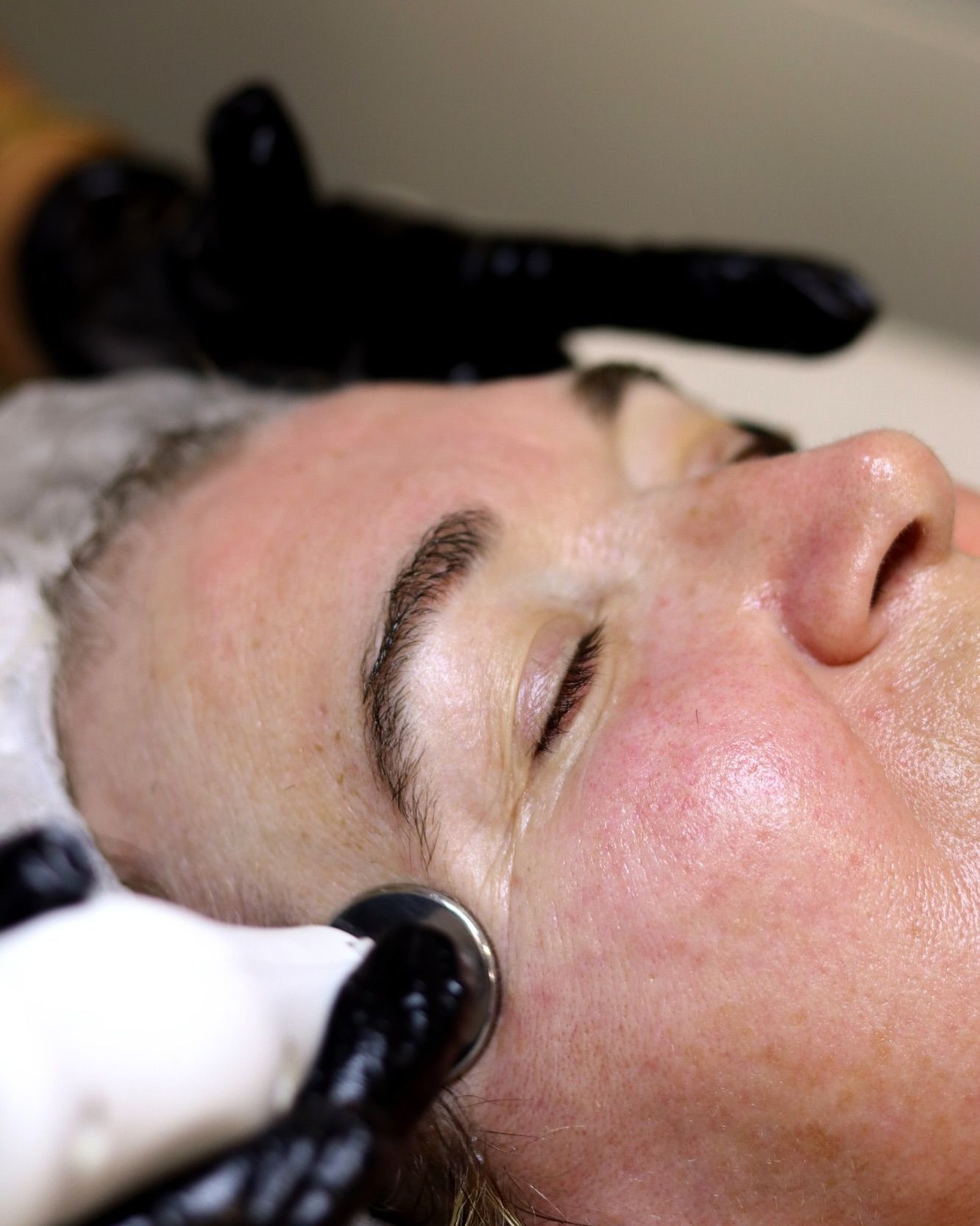 Una mujer está recibiendo un tratamiento facial con los ojos cerrados.
