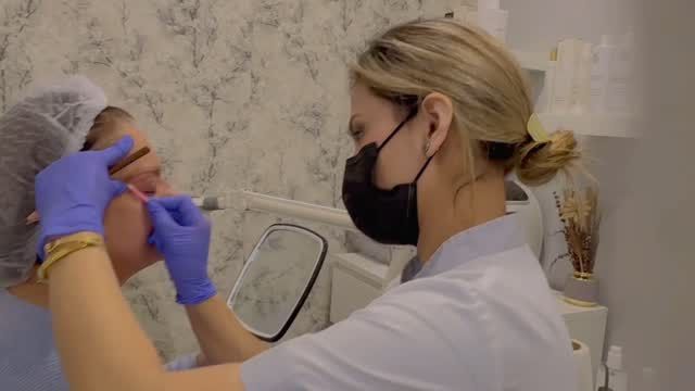 Una mujer que lleva una máscara y guantes está aplicando maquillaje en la cara de otra mujer.