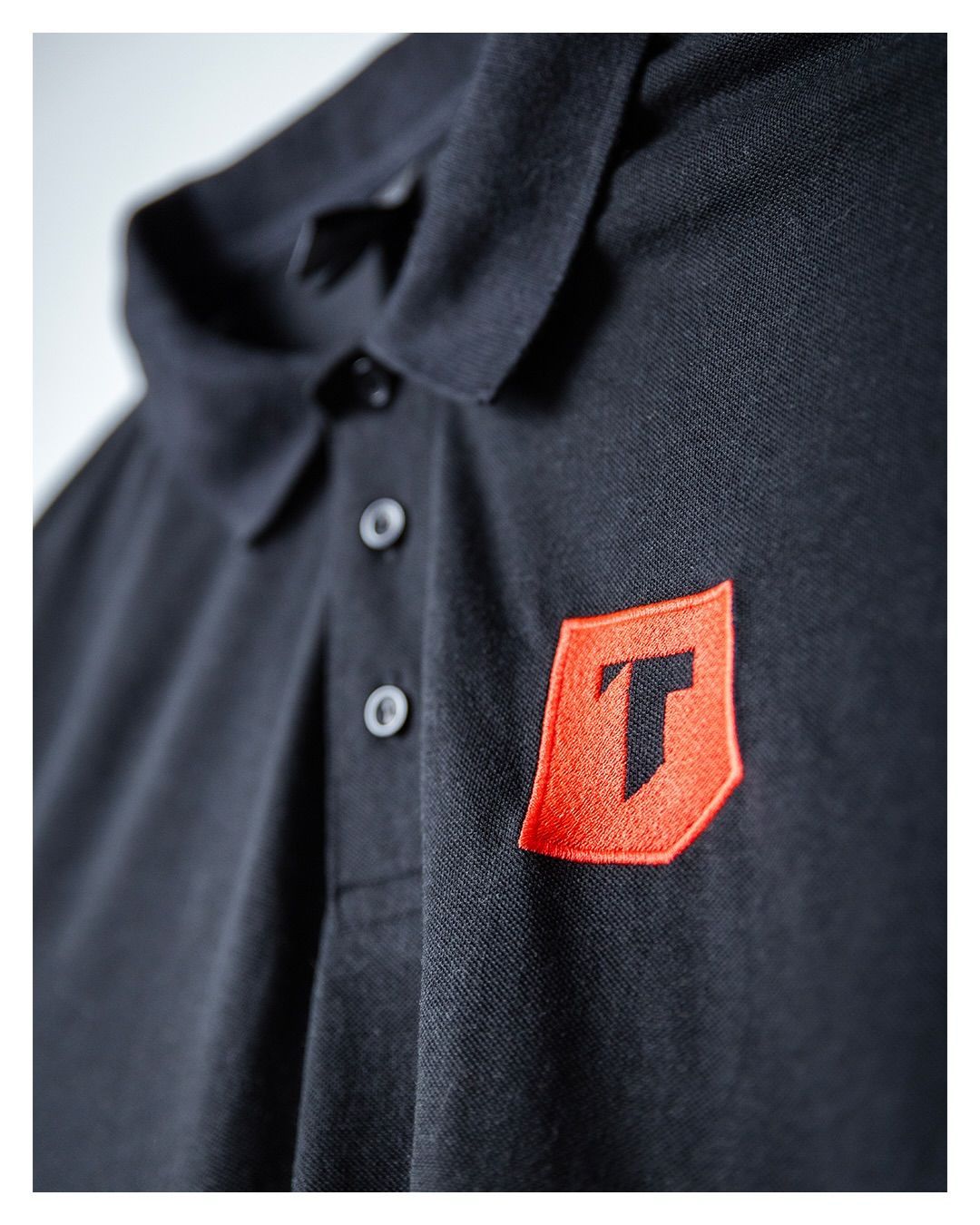 Polo noir avec un écusson rouge sur la poitrine et un T