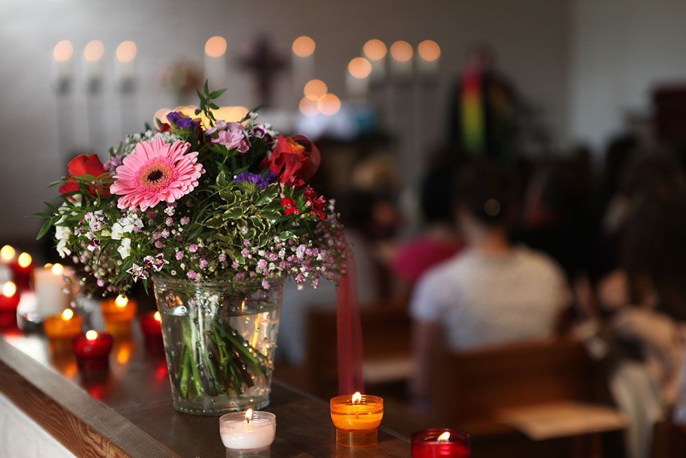 Vase mit Blumen, brennenden Kerzen und Menschen in der Kirche. Konzentrieren Sie sich auf die Blumen und Kerzen.