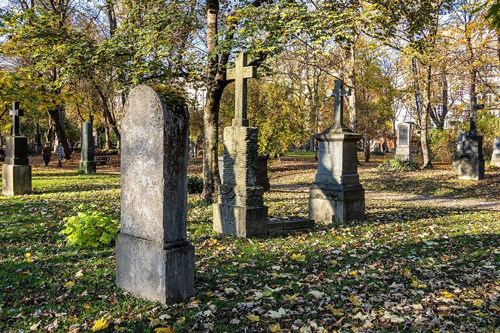 Friedhof mit Grabsteinen, Kreuzen und Bäumen im Herbst.