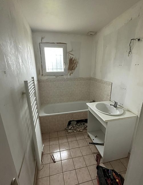 Petite salle de bains défraîchie avec une baignoire, un meuble lavabo, un sol carrelé et une fenêtre au-dessus de la baignoire