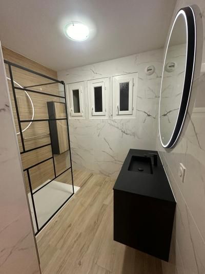 Salle de bains moderne avec douche vitrée, murs effet marbre, puits de lumière, miroir rond et meuble-lavabo noir.
