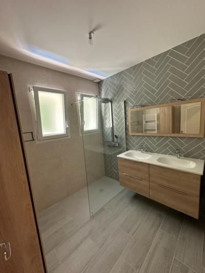 Salle de bains moderne avec double vasque, douche à l’italienne, carrelage mural gris à chevrons et fenêtre dépolie