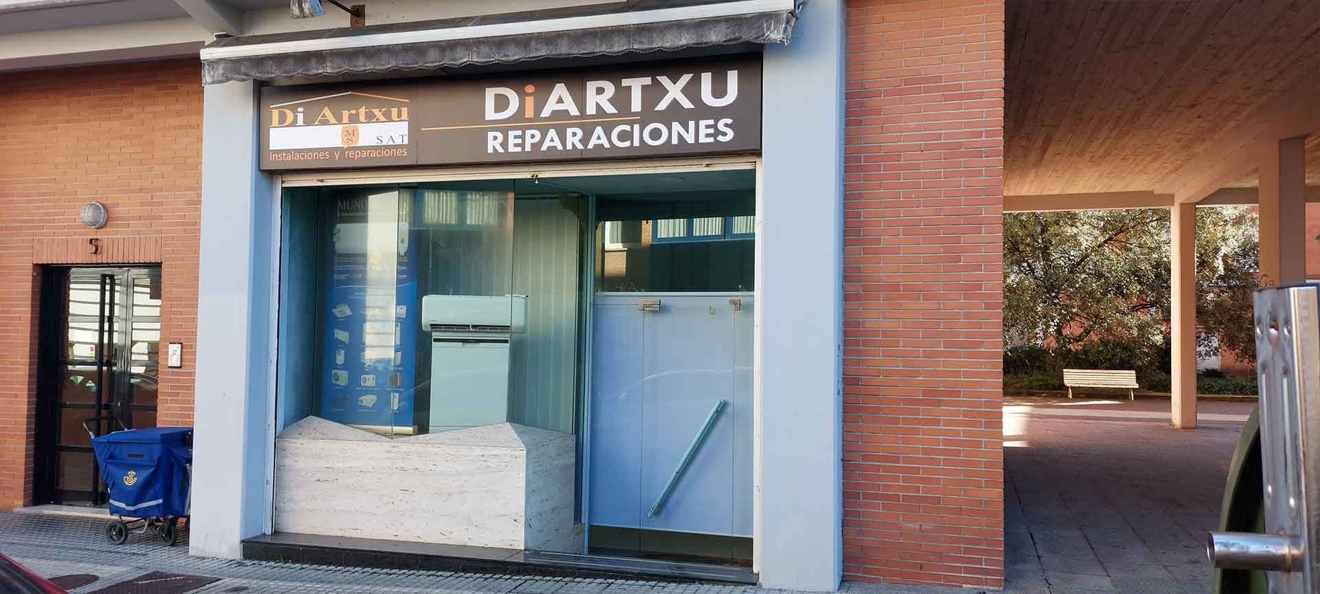Vista exterior de un taller de reparaciones llamado DIARTXU con puerta metálica cerrada y materiales de construcción.