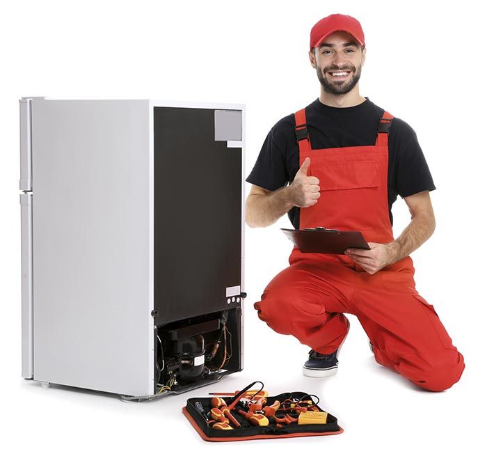 Reparador de refrigeradores con mono rojo y gorra haciendo un gesto de aprobación con el pulgar, arrodillado junto al refrigerador y las herramientas.