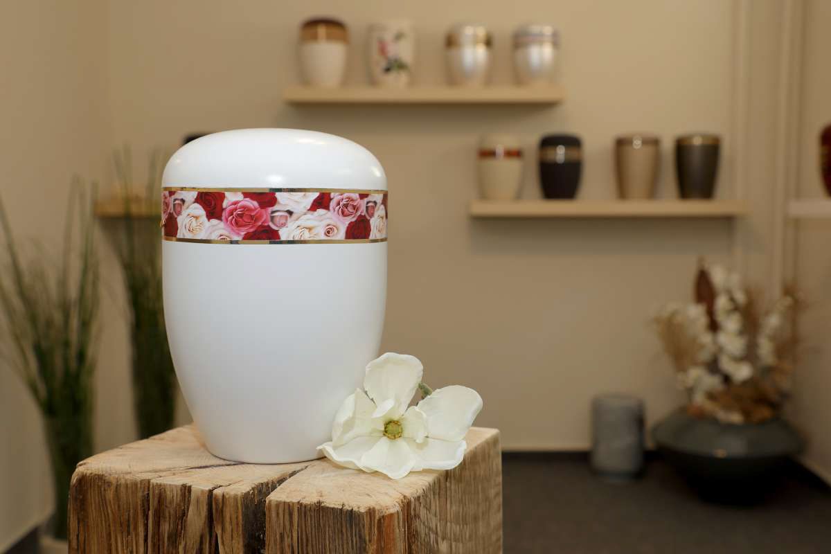Eine weiße Urne mit einer Blume darauf steht auf einem Holzblock.