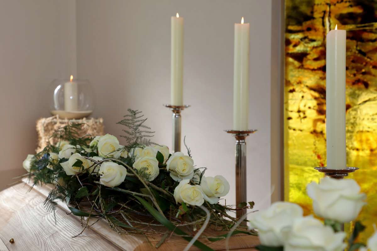 Ein Sarg ist mit weißen Rosen und Kerzen geschmückt