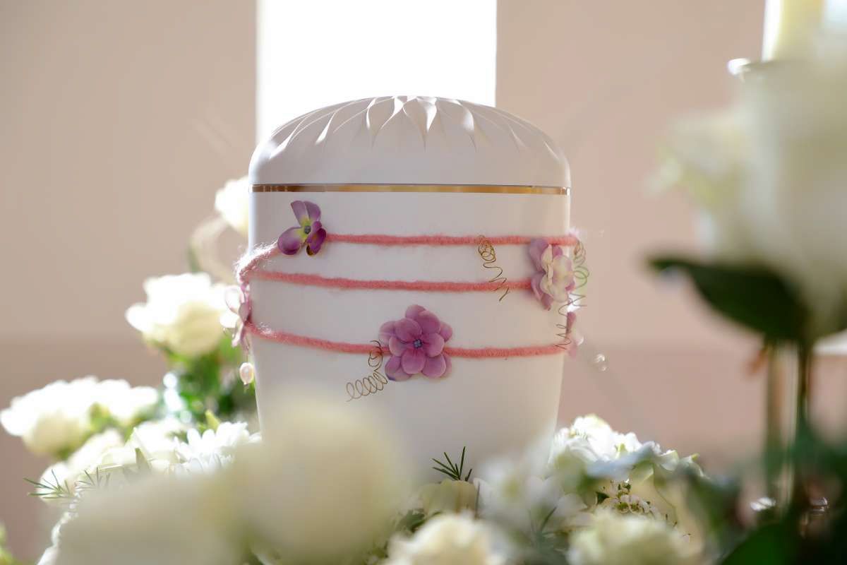 Eine weiße Vase mit rosa Blumen steht auf einem Tisch, umgeben von weißen Blumen.