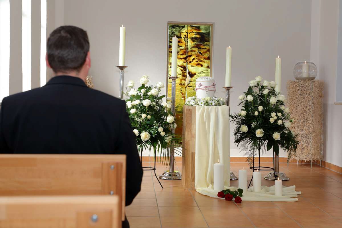 Ein Mann sitzt in einer Kirche und betrachtet Blumen und Kerzen.