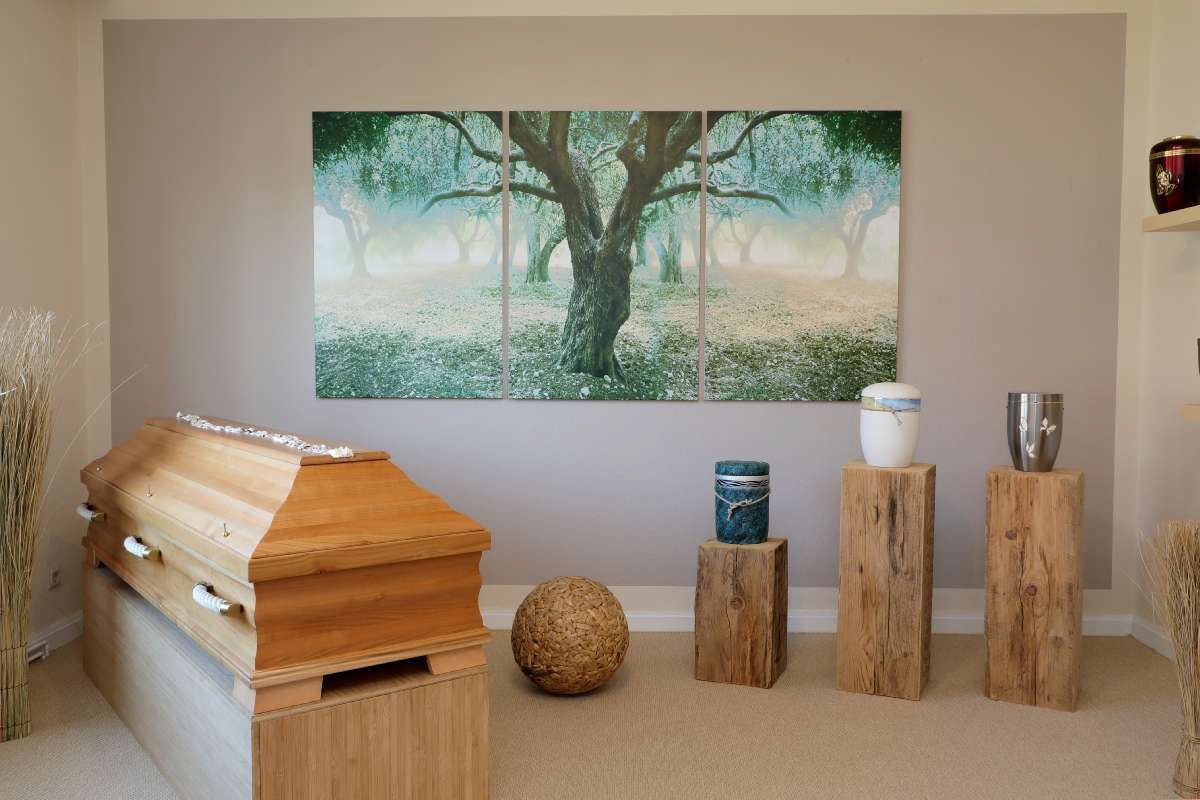 Ein Raum mit einem Sarg, Urnen und einem Baumgemälde an der Wand.