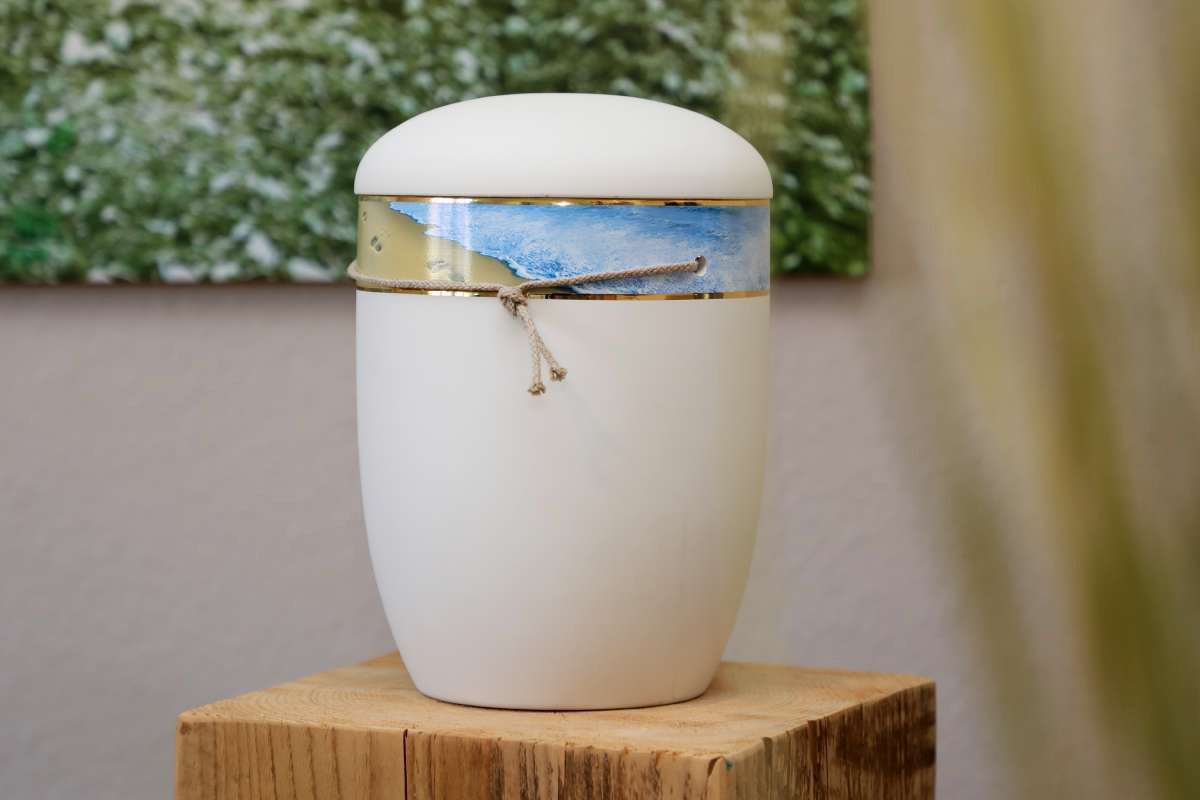 Eine weiße Urne steht auf einem Holzblock.