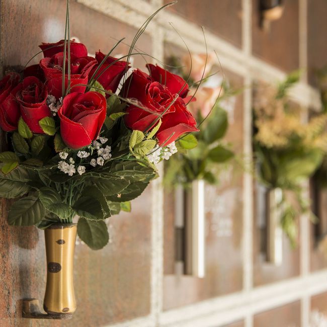 Ein Strauß roter Rosen hängt an einer goldenen Vase auf einem Friedhof.