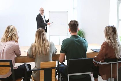 Ein Mann hält vor einer Gruppe von Leuten, die an einem Tisch sitzen, eine Präsentation.