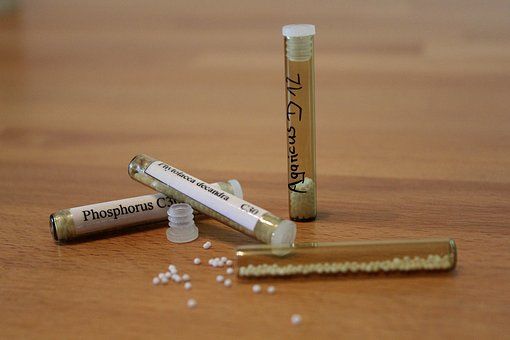 Drei Tuben mit homöopathischen Arzneimitteln stehen auf einem Holztisch.