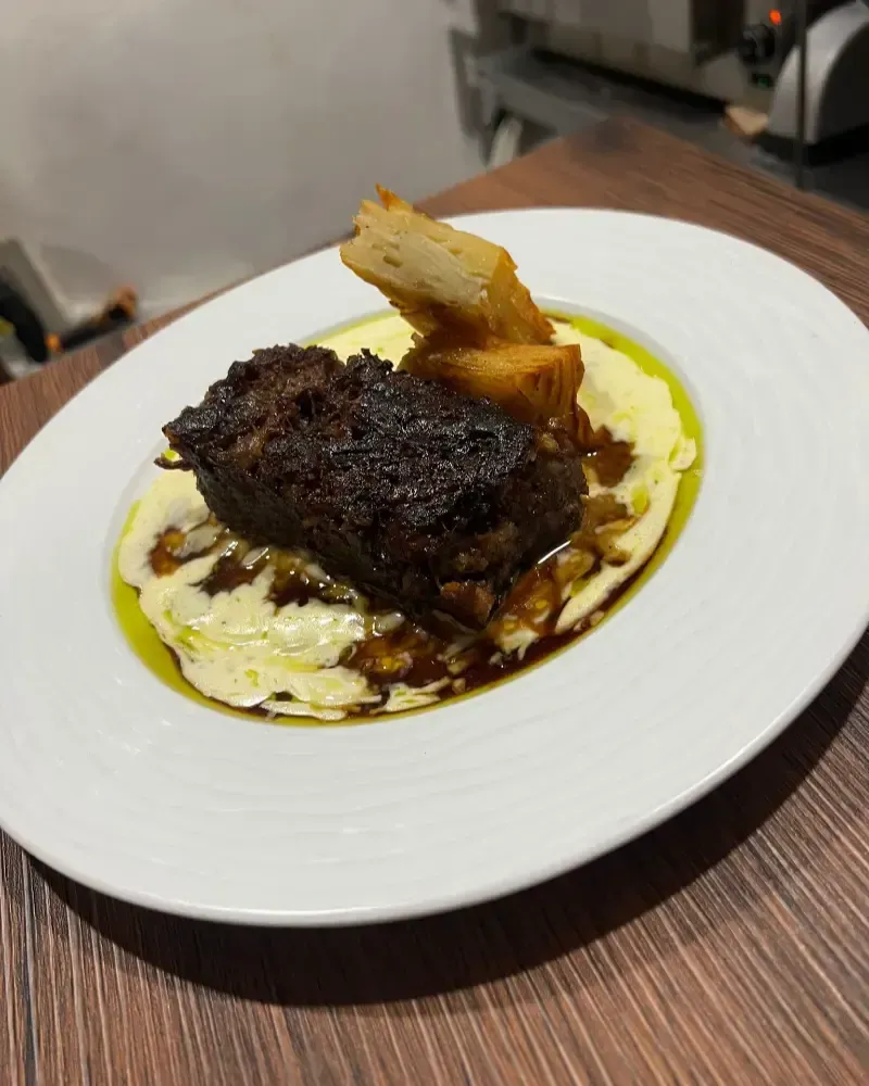 Filete emplatado con salsa y puré de patatas cremoso en un plato blanco sobre una mesa de madera.