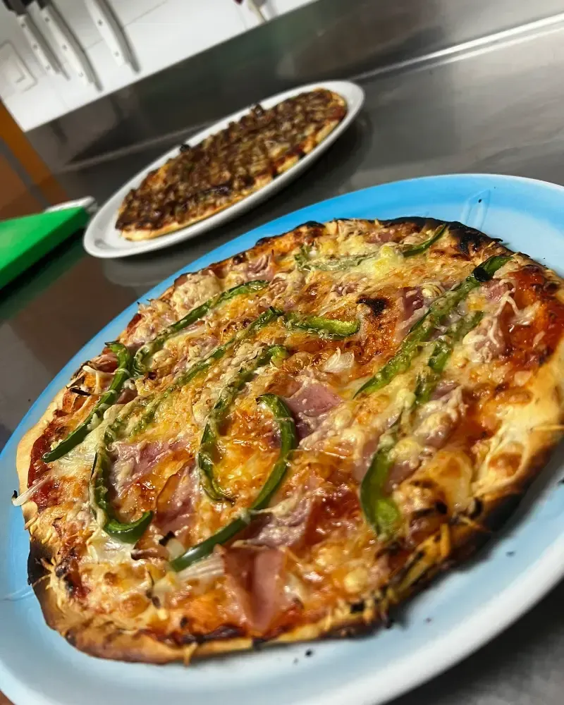 Dos pizzas en platos en una cocina, una de ellas con pimientos verdes y queso fundido en primer plano.