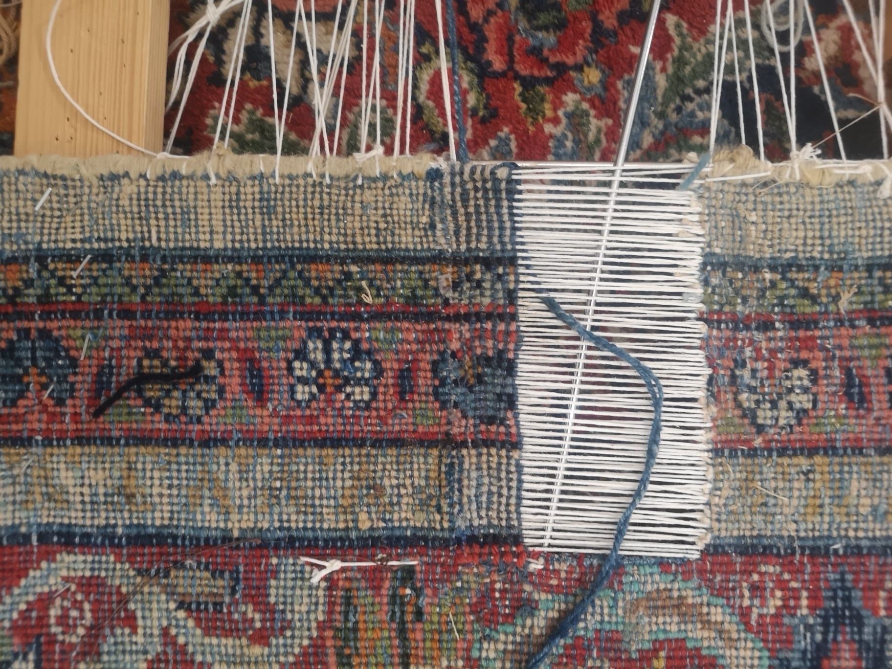 Gros plan d’un tapis tissé avec une couture de réparation blanche et un fil bleu traversant un tissu à motifs.