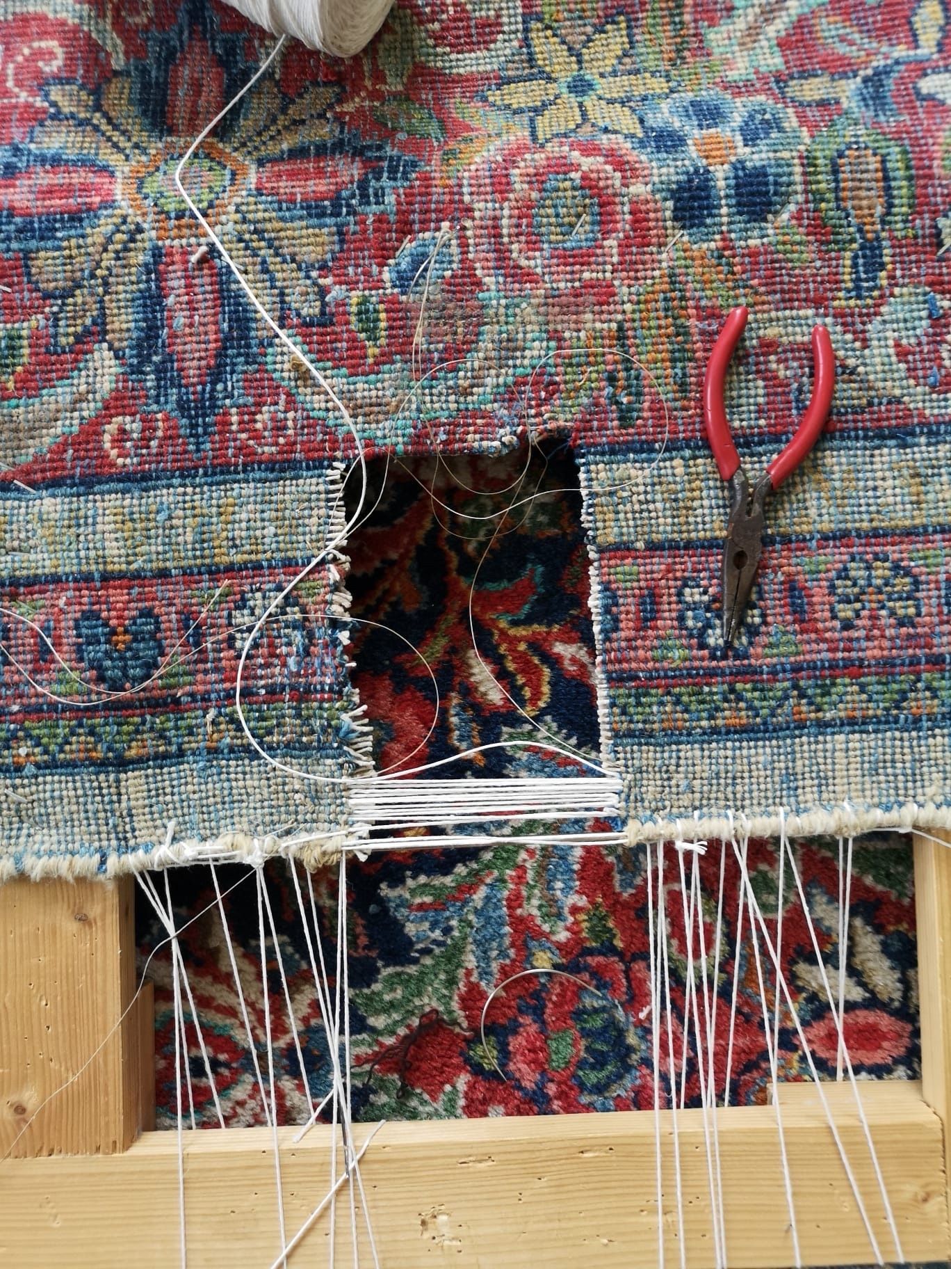 Gros plan sur un tapis à motifs déchiré en cours de réparation, avec une pince à côté de la zone endommagée.