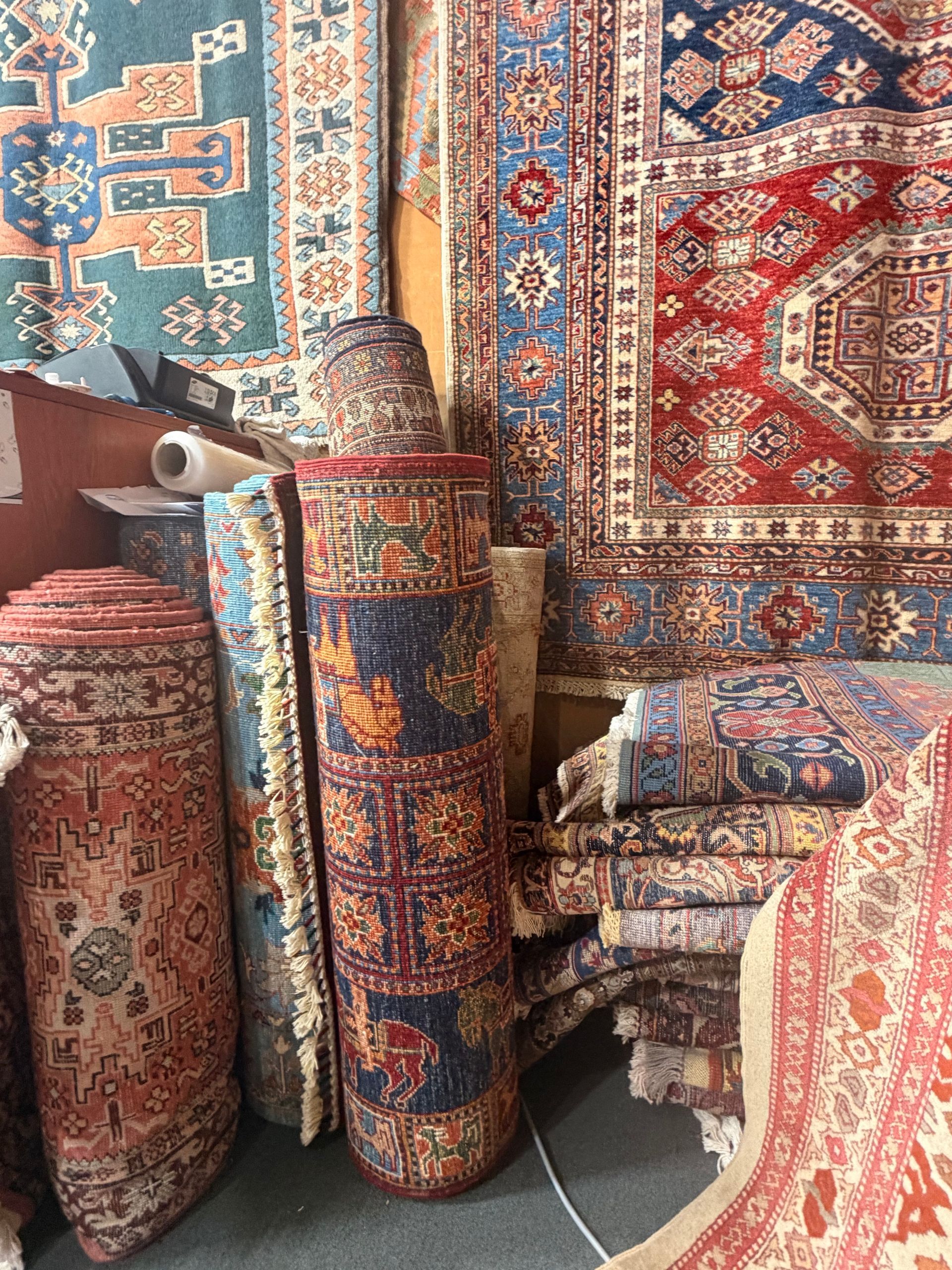 Tapis vintage roulés sur un marché, aux motifs persans colorés rouges, bleus et dorés
