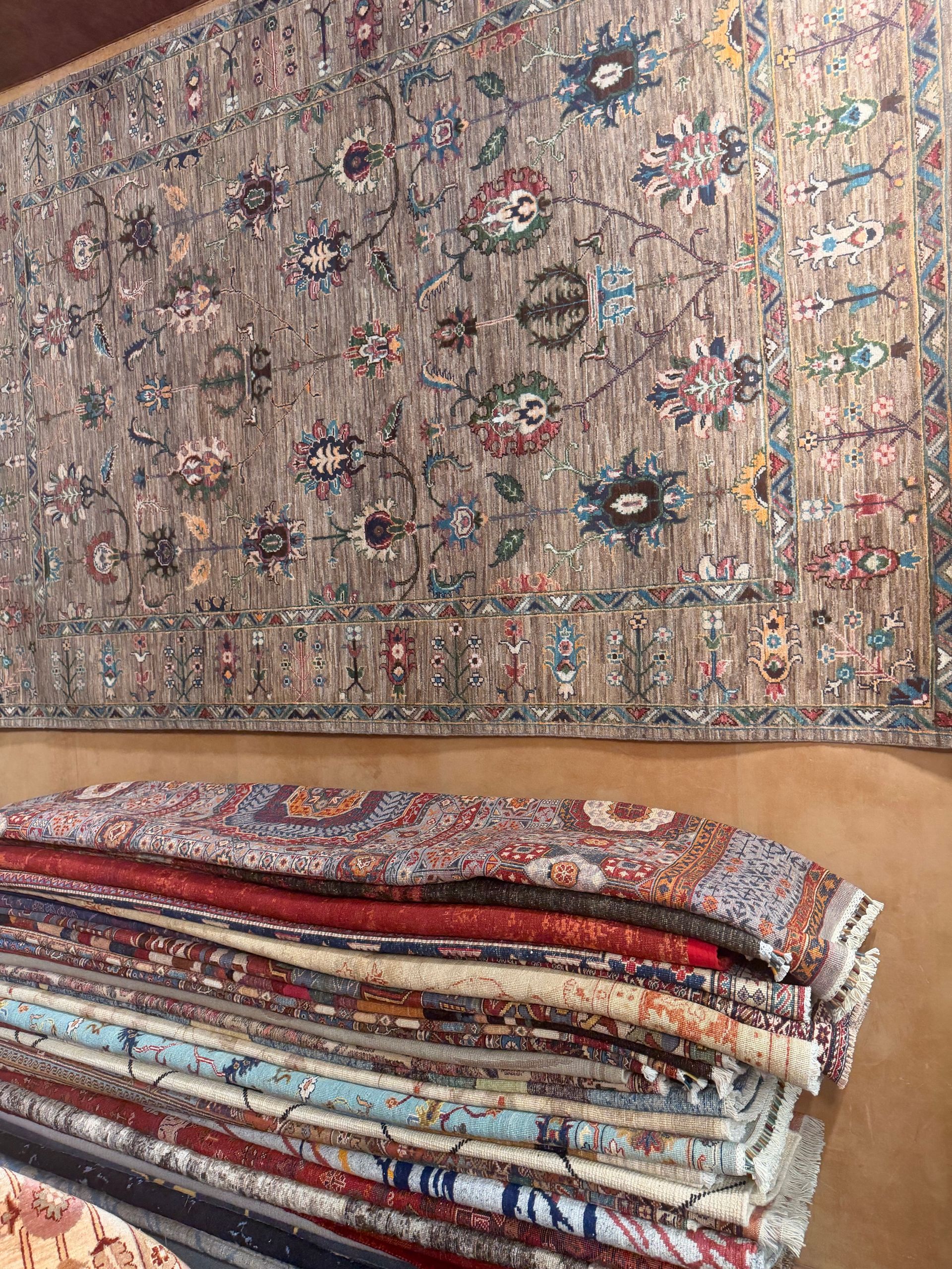 Des textiles pliés à motifs, empilés sous un grand tapis orné multicolore, sur un sol beige