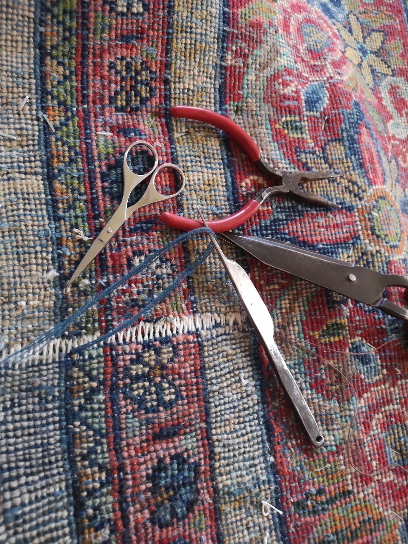 Trois paires de ciseaux, dont une à manche rouge, posées sur un tapis à motifs