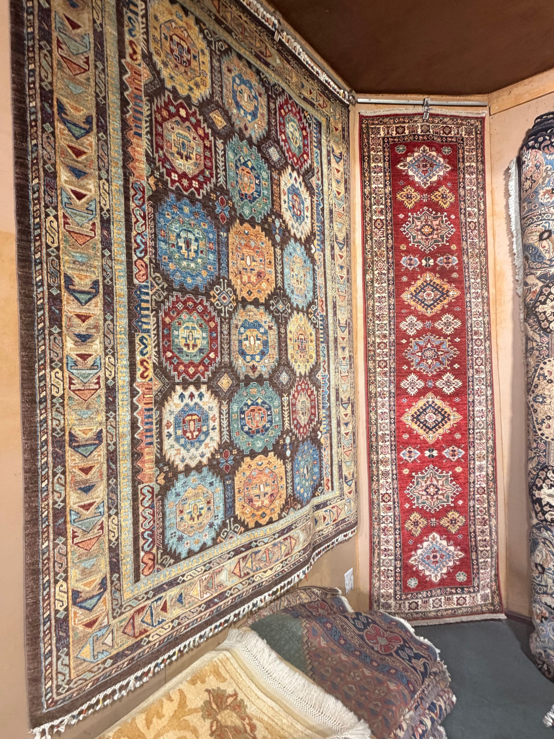 Des tapis colorés à motifs accrochés dans un coin de mur, au-dessus d’un petit tapis posé au sol.