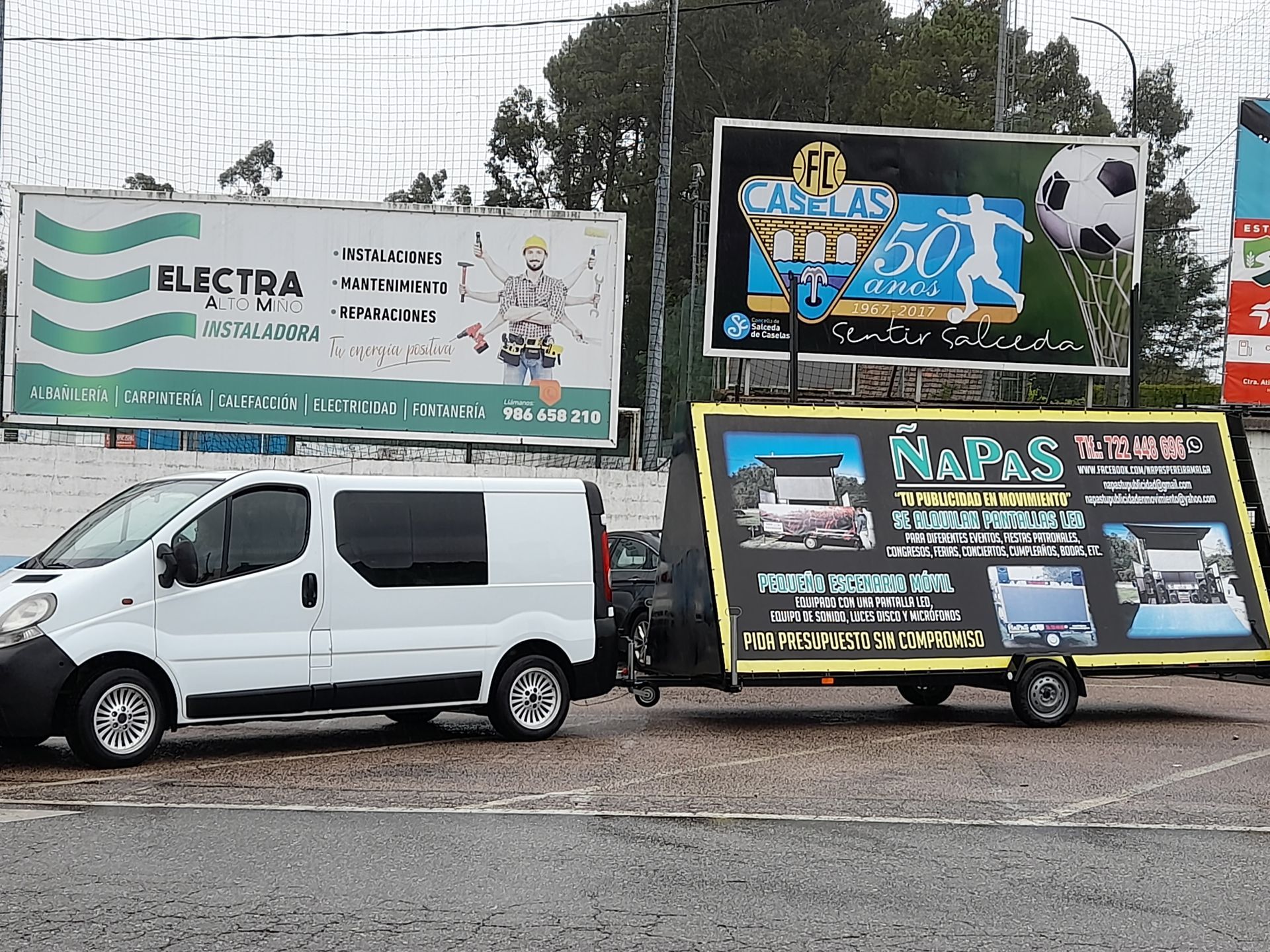 Una camioneta blanca con un remolque acoplado está estacionada frente a una valla publicitaria de Electra.