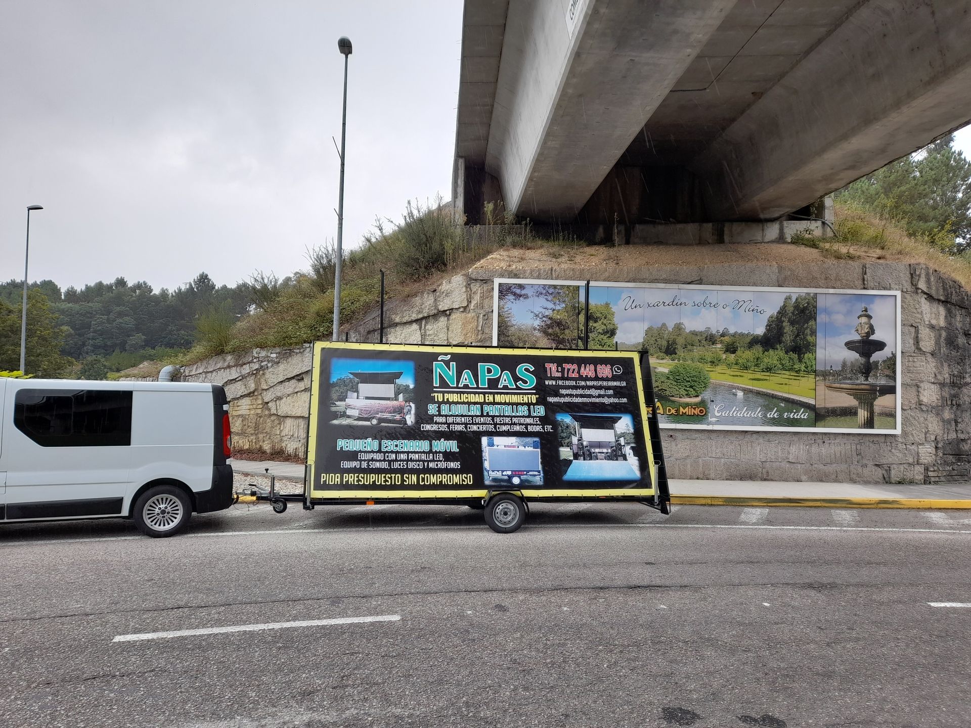 Una camioneta blanca está estacionada debajo de un puente junto a un cartel que dice mapas