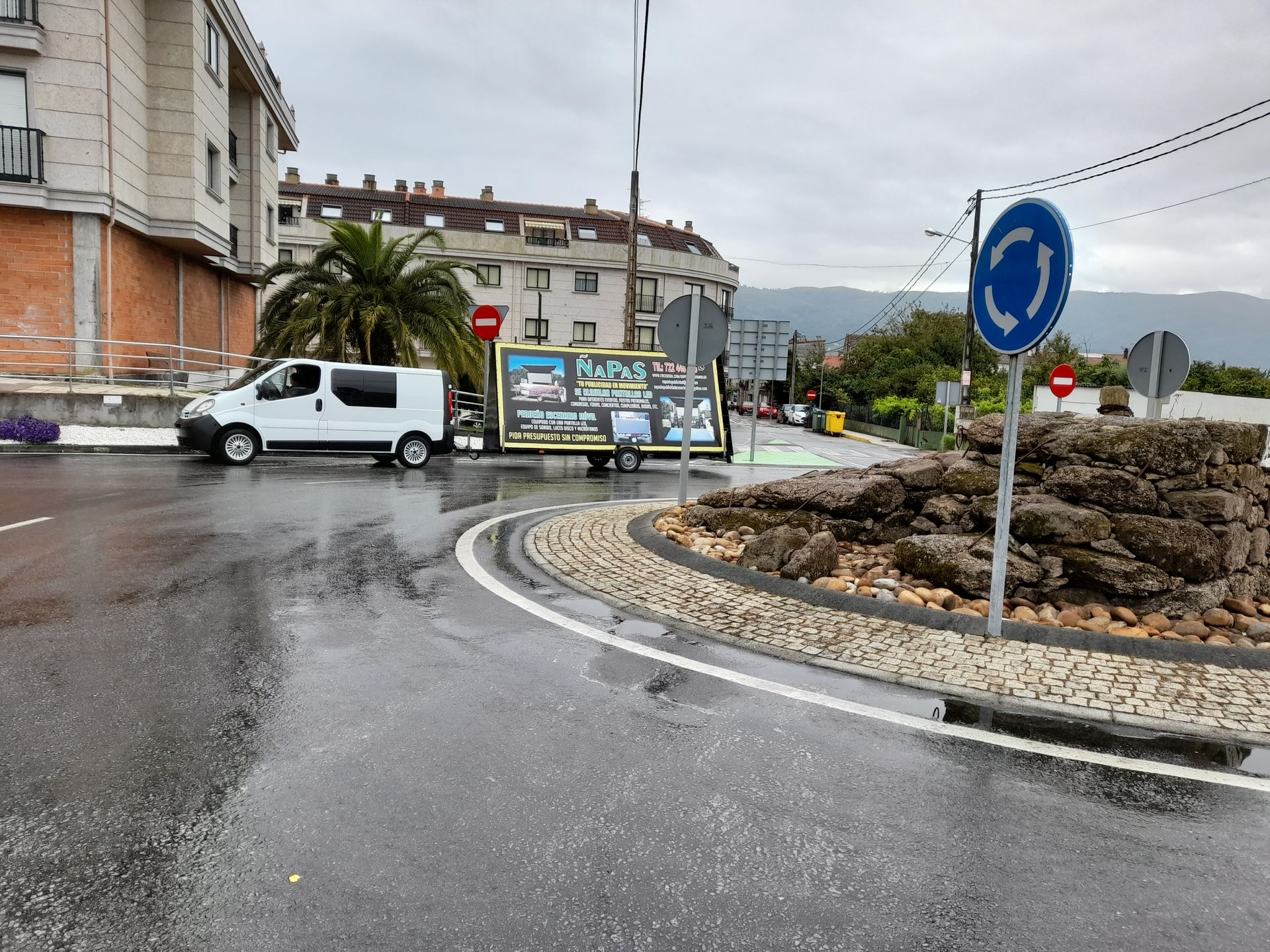 Una furgoneta blanca circula por una rotonda bajo la lluvia.