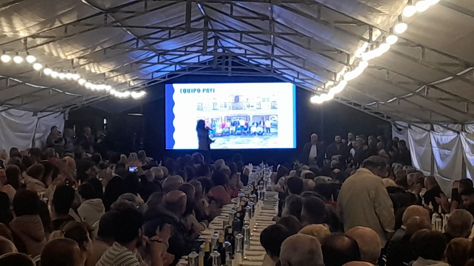 Un grupo grande de personas está sentado en una mesa larga frente a una pantalla grande.