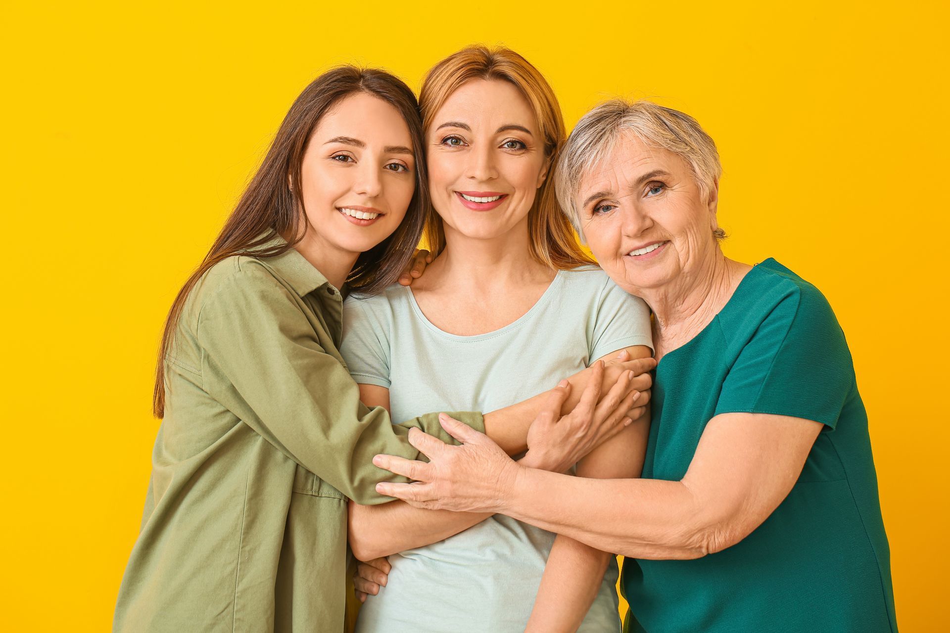Trois femmes souriantes et enlacées sur fond jaune.
