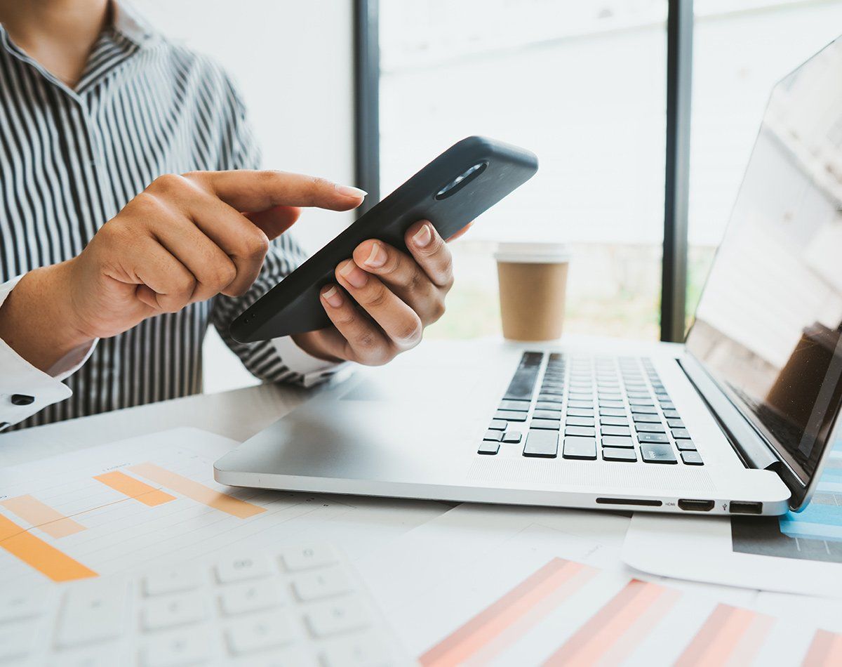 Main utilisant un téléphone portable au-dessus d'un ordinateur portable