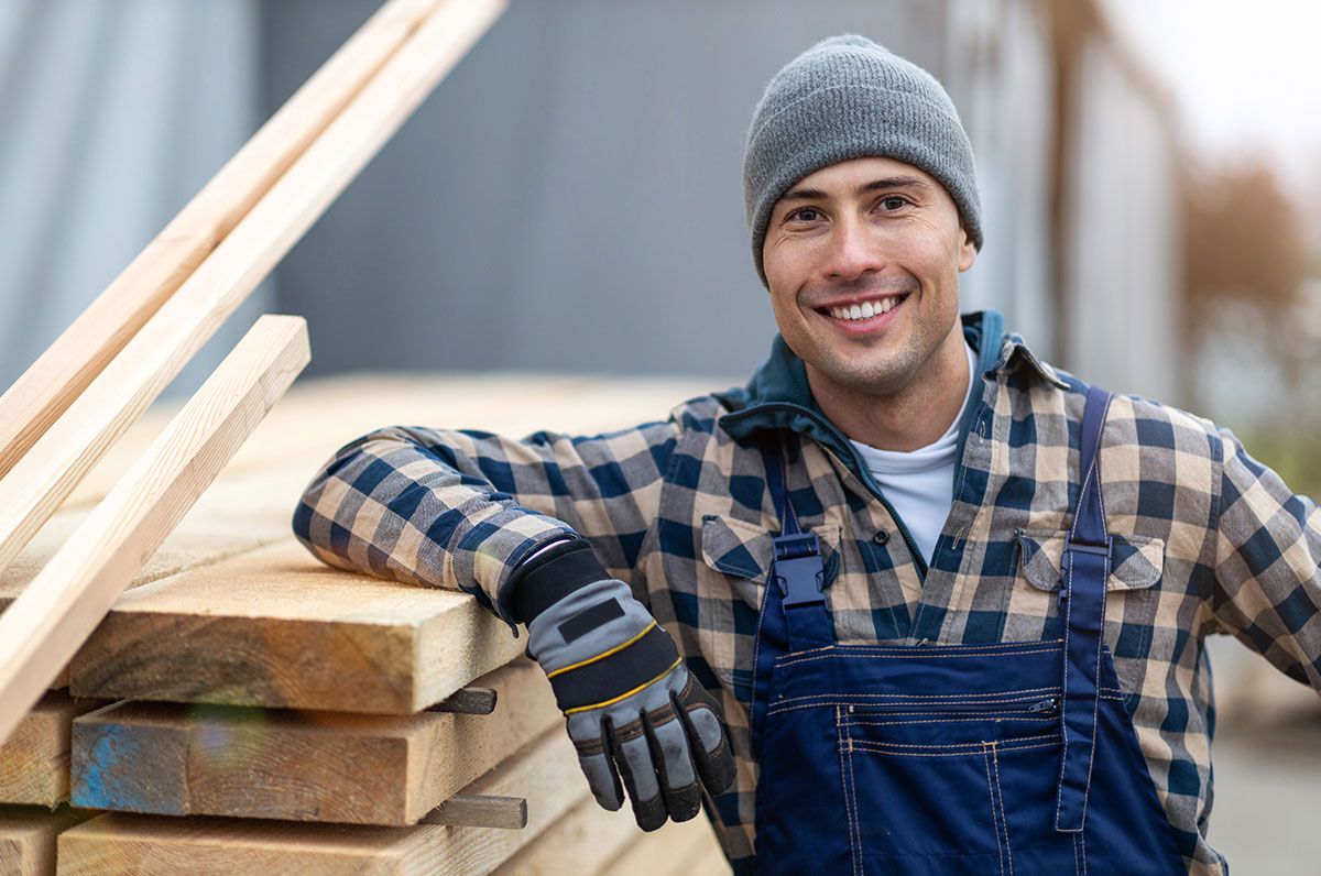 Ouvrier souriant appuyé sur une pile de bois de charpente