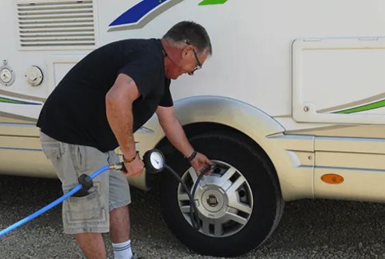 Un homme penché en avant regonfle le pneu d'un camping-car
