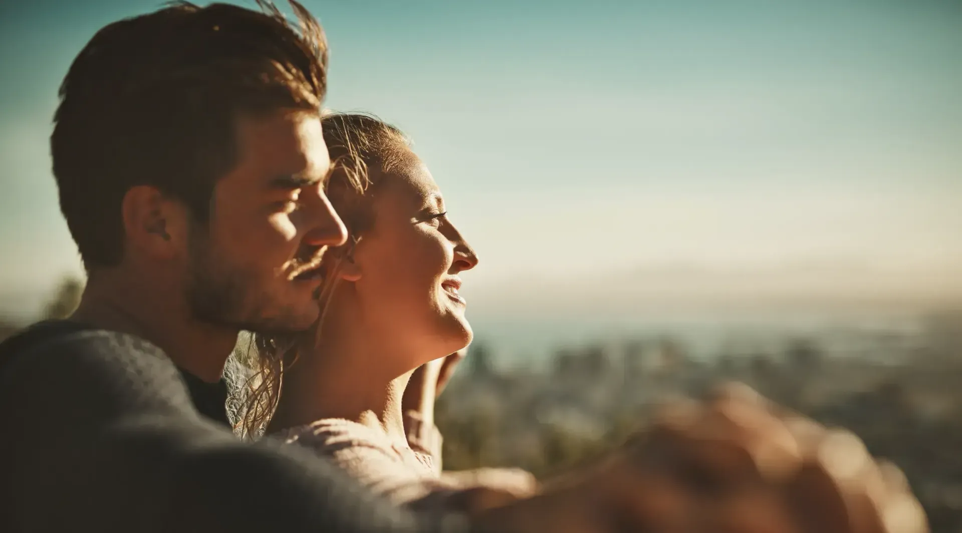 Un hombre y una mujer se abrazan, mirando un paisaje urbano bajo un cielo soleado.