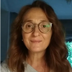 Mujer con gafas, piel clara y cabello ondulado de color rojo, mirando directamente a la cámara.