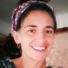 Mujer con ojos marrones y sonrisa que lleva una diadema estampada y pendientes de aro.