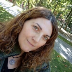 Mujer con cabello castaño rizado, ojos verdes, sonriendo al aire libre en el parque, llevando un collar.