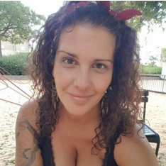 Mujer con cabello castaño rizado, diadema roja, sonriendo, al aire libre, tatuaje en el brazo.