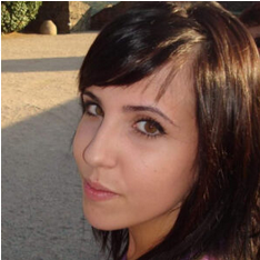 Mujer de cabello y ojos castaños mira hacia la cámara, al aire libre, bajo la luz del sol.