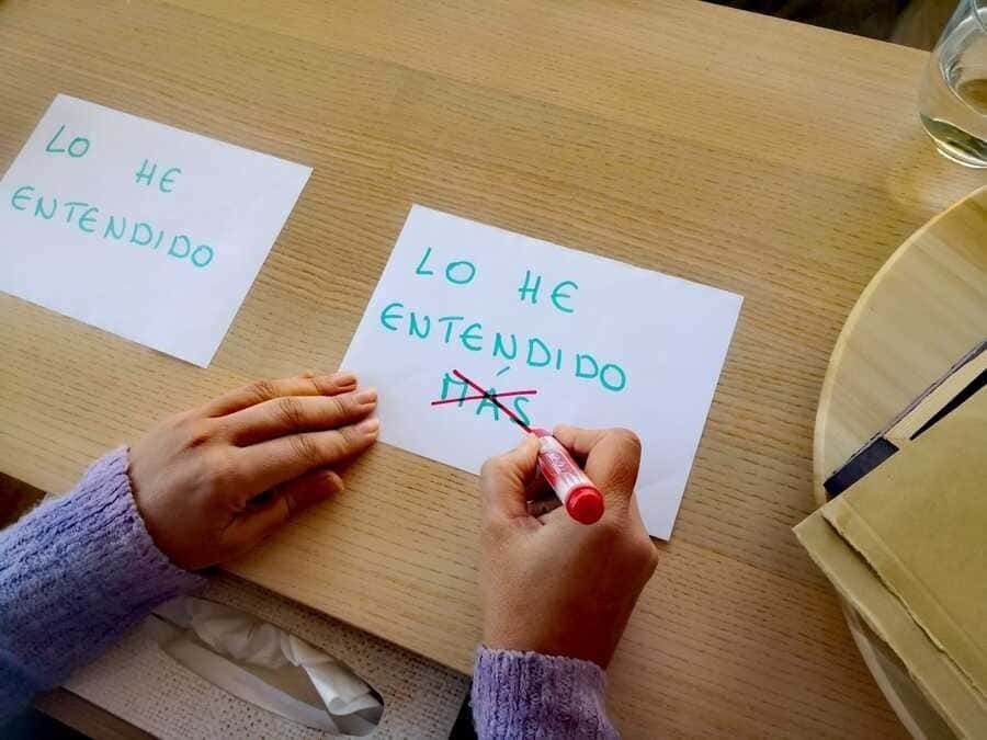 Las manos de una persona tachando "yo" en la frase "LO HE ENTENDIDO" en un papel con un marcador rojo.