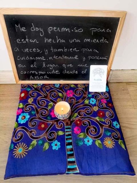 Una pizarra con texto en español, una vela y un mantel floral de colores. El texto dice: "A veces me permito ser un desastre..."