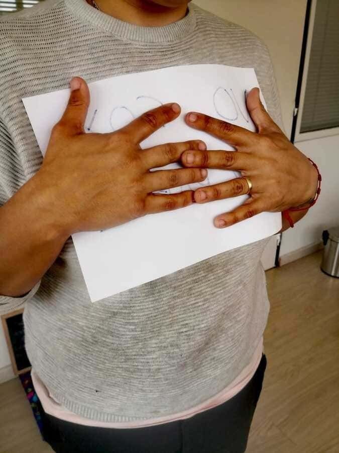 Persona sostiene un papel con las manos cubriendo el pecho, viste un suéter gris.