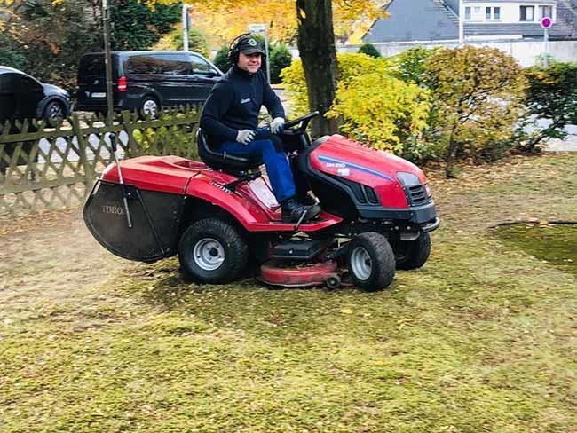 Ein Mann fährt mit einem Rasenmäher über einen üppigen grünen Rasen.