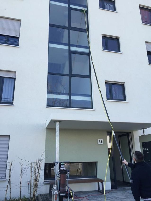 Ein Mann putzt die Fenster eines Gebäudes mit einer langen Stange