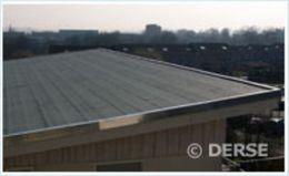 Nahaufnahme eines dunkelgrauen Flachdachs mit metallisch glänzender Kante vor verschwommenem urbanem Hintergrund.