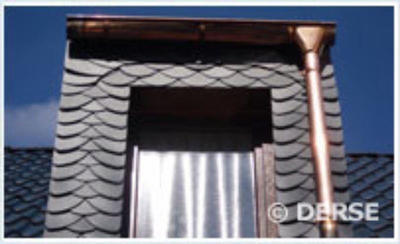 Ein Dachgaubenfenster, verkleidet mit dekorativen Schieferfliesen in Fischschuppenoptik, mit einer Kupferrinne und Fallrohr